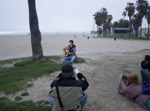 Greg Koons playing guitar on Venice Beach as photographers shoot