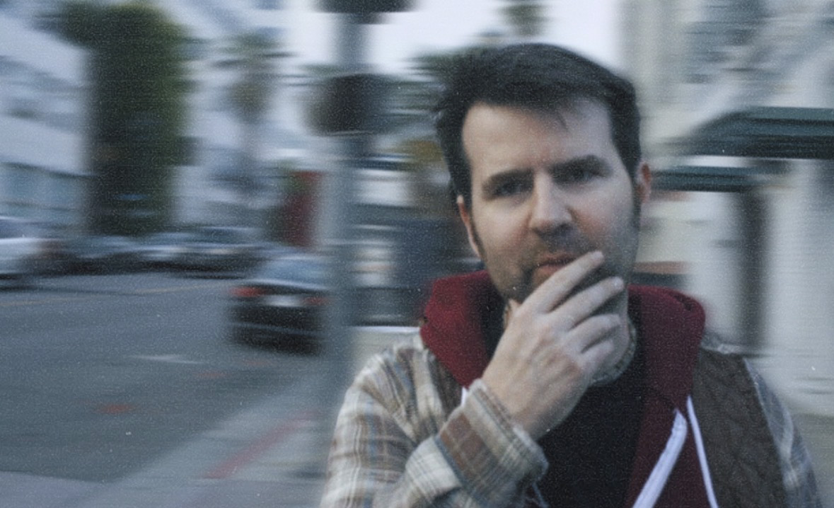 Greg Koons on a city street, motion-blurred traffic behind him